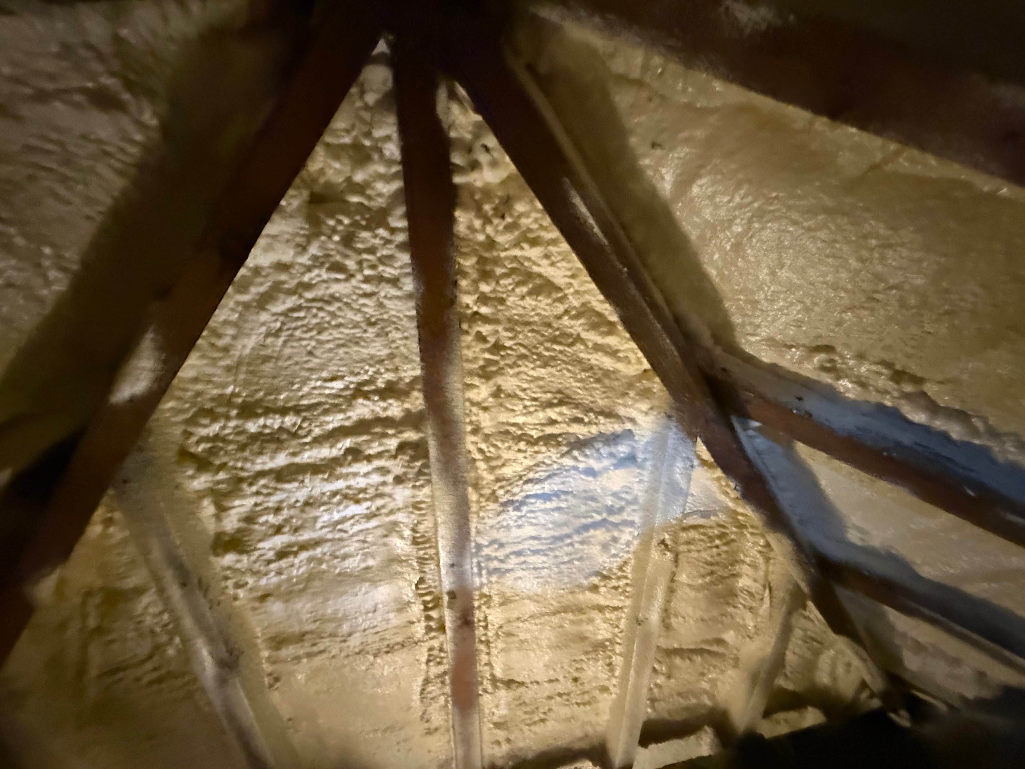 Dense closed-cell spray foam coating roof rafters — hard, cream-coloured and rigid